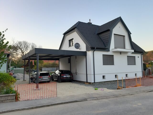 Vordach- und Carportkonstruktion aus Metall mit Glaseindeckung an einem Wohnhaus
