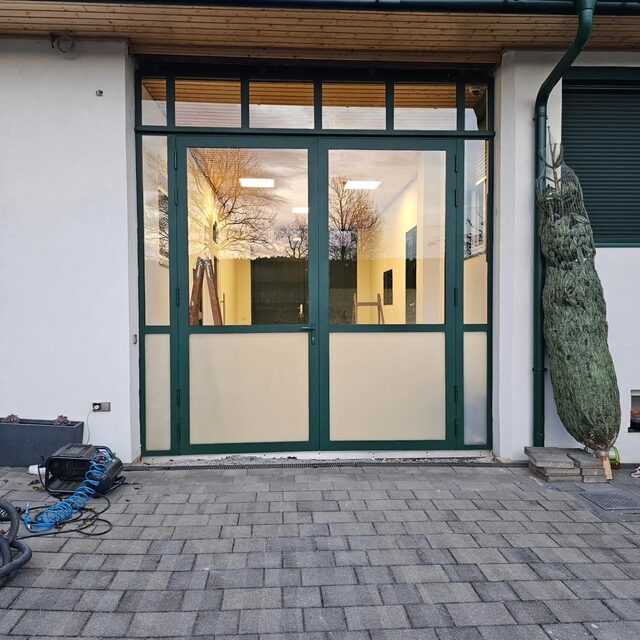 Grün lackiertes Metall-Glasportal als Eingangstür zu einem Gebäude
