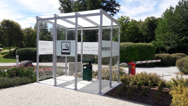 Freistehender Raucherpavillon aus Metall und Glas auf einem Firmengelände