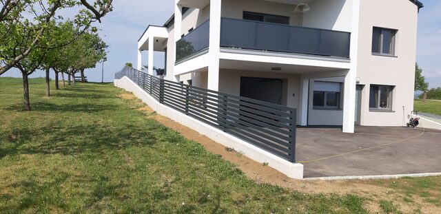 Aluminium-Lamellenzaun auf einer Betonmauer an einem Hanggrundstück