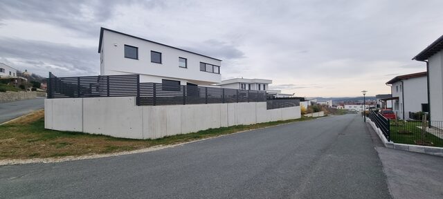 Anthrazitfarbener Lamellenzaun auf Betonmauer an einem modernen Wohnhaus